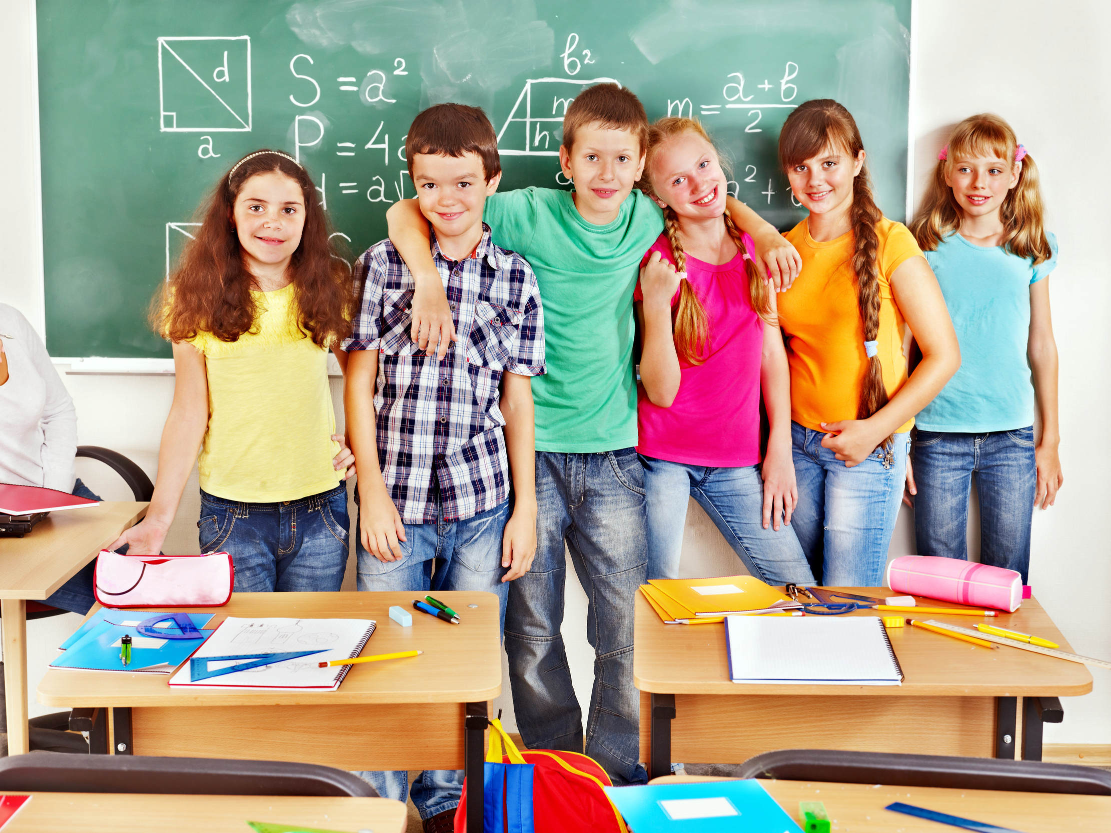 Group of school child sitting on desk in classroom.